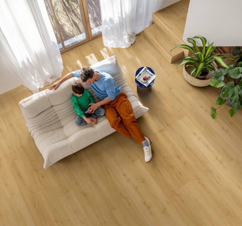 lvt-floor-quick-step-bloom-brushed-oak-honey LVT floor Quock-Steü Bloom Brushed Oak Honey installed on the Livingroom floor: Father and son watching a phone on a sofa.
