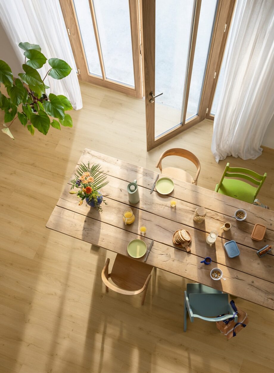 rigid-vinyl-quick-step-bloom-brushed-oak-honey Rigid Vinylboden Quick Step Bloom Brushed Oak Honey im Esszimmer verlegt, Esstisch und Stühle, Blumen, Frühstück auf dem Tisch.