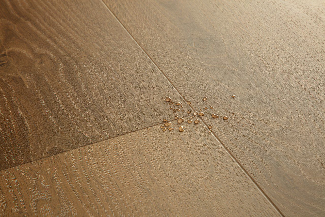 Vinyylilankku Quick Step Bloom Elegant Fumed Oak, tumma savutammen sävy ja lankkudesign, pinnalla vesipisaroita korostamassa lattian vedenkestävyyttä.