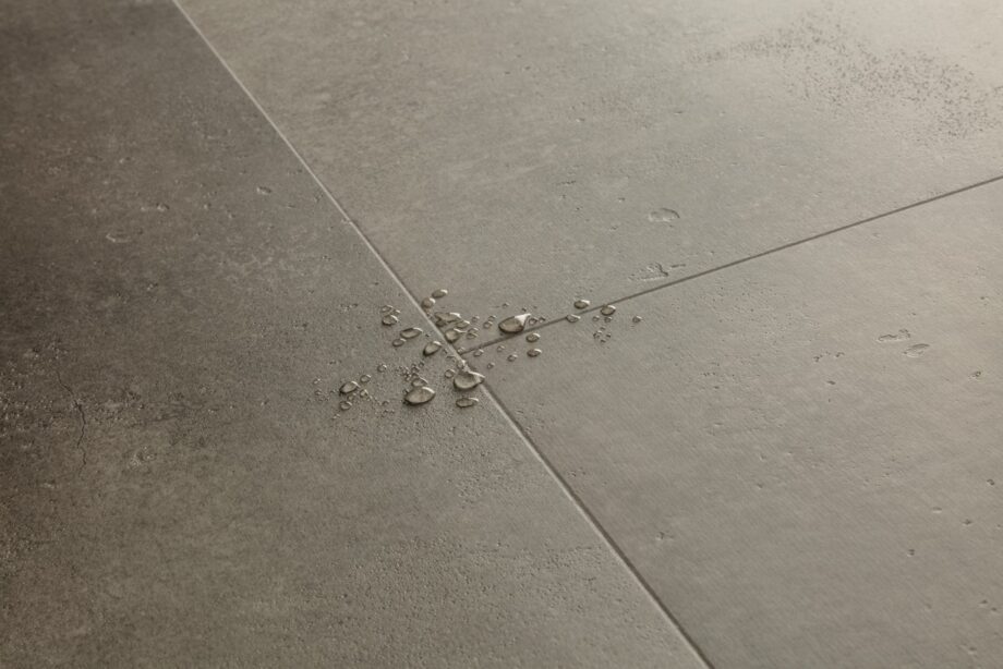 lvt-parkett-quick-step-illume-cloudy-concrete LVT parkett Quick-Step Illume Cloudy concrete tumehalli tooni ja betooni disainiga. Põrandal on veepiisad viitamaks antud LVT parketi veekindlusele.