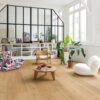 klick-vinyl-quick-step-bloom-elegant-oak-natural Klick Vinyl Quick Step Bloom Elegant Oak Natural im Wohnzimmer verlegt, Sessel, Tisch, Regal und Topfpflanzen.