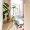 Klick Vinylboden Quick Step Bloom Brushed Oak Beige im Schlafzimmer verlegt, mit Palme, rosa Sitzhocker, rosa Vorhängen und Bett.