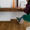 lvt-flooring-quick-step-bloom-botanic-caramel-oak LVT flooring Quick-Step Bloom Botanic Caramel Oak installed on a living room floor. Woman is sitting on a stool.