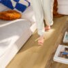 lvt-flooring-quick-step-bloom-brushed-oak-honey LVT flooring Quick-Step Bloom brushed oak honey installed on a livingroom floor. Woman walking on the floor, sofa and sofa table.