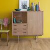 rigid-vinyl-quick-step-bloom-cotton-oak-natural Rigid Vinylboden Quick Step Bloom Cotton Oak Natural im Wohnzimmer verlegt, gelbe Wand und klassischer Vitrinenschrank.