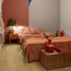 Vinüülprkett Quick-Step Bloom Cotton Oak Deep Natural paigaldatud magamistoa põrandale. Voodi, öökapp, lamp ja lill öökapil, kummut millel raamat ja vaas lilledega.