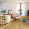 vinyl-floor-quick-step-bloom-brushed-oak-honey Vinyl floor Quick-Step Bloom Brushed Oak Honey installed on a living room floor. Sofa, table, flowers.