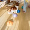 vinyl-quick-step-bloom-brushed-oak-honey Vinylboden Quick Step Bloom Brushed Oak Honey im Wohnzimmer verlegt, Kind spielt mit einem Hund.