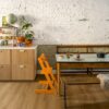 vinylböden-quick-step-bloom-botanic-caramel-oak Vinylboden Quick Step Bloom Botanic Caramel Oak im Esszimmer verlegt, orangefarbener Kinderstuhl, Esstisch, Schränke und Blumen.