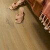 Vinyylilattia Quick Step Bloom Cotton Oak Deep Natural asennettuna makuuhuoneen lattialle, syvä luonnollinen tammen sävy ja lankkudesign, sänky ja kengät lattialla.