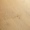 vinyylilattia-quick-step-bloom-elegant-oak-natural Vinyylilattia Quick Step Bloom Elegant Oak Natural, luonnollinen tammen sävy ja lankkudesign, pinnalla vesipisaroita korostamassa lattian vedenkestävyyttä.