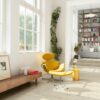Vinyylilattia Quick Step Blos Vaalea Canyon Tammi Beige asennettuna olohuoneen lattialle ja kirjanurkkaan johtaville porrasaskelmille, vaalea hiekanbeige tammen sävy ja lankkudesign, keltainen lepotuoli jalkarahilla, lipasto sekä hyllyjä kirjoineen.