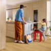 виниловыи-ламинат-quick-step-bloom-brushed-oak-honey Виниловый ламинат Quick Step Bloom Brushed Oak Honey уложен на полу на кухне, отец и дочь у кухонного острова, рядом собака.