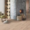 lankkuparketti-bauwerk-boen-casapark-tammi-46-harjattu-vaalea-farina-oljyvahattu Lankkuparketti Bauwerk Boen Casapark tammi 46 Farina, harjattu ja öljyvahattu, asennettuna olohuoneen lattialle – suuri, harmaalla kivellä verhoiltu lämmitettävä takka, vihreä nojatuoli ja polkupyörä. Vaalea Farina-sävy ja rustiikkinen sorteerus tuovat esiin tammen eläväisen kuvioinnin.