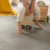 lvt-parkett-quick-step-oro-concrete-rock LVT parkett Quick-Step Oro Concrete rock paigaldatud lastetoa põrandale. Laps istub ratastega tumbal.