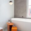 lvt-plaat-quick-step-oro-concrete-rock LVT plaat Quick-Step Oro Concrete rock paigaldatud vannitoa põrandale. Eraldiseisev valge vann, oranzh tarvikute laud.