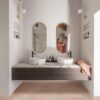 LVT Quick-Step Illume Soft blush paigaldatud vannitoa põrandale. Topelt vannitoamööbel valgest marmorist tasapinnaga millel kaks stiilset tasapinnapealset valamut. Seinapeeglist paistab naisterahvas.
