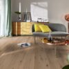 tammiparketti-bauwerk-boen-casapark-tammi-46-vivo-harjattu-avorio-vaalea-oljyvahattu Tammiparketti Bauwerk Boen Casapark tammi 46 Vivo Avorio, harjattu ja öljyvahattu, asennettuna olohuoneen lattialle – minimalistinen sohva ja pyöreä sohvapöytä kuparinvärisellä tasolla. Vaalea Avorio-sävy ja rustiikkinen sorteerus tuovat esiin tammen eläväisen kuvioinnin.