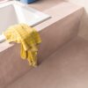 Vinyl flooring tiles Quick-Step Illume Soft blush installed on bathroom floor. Built in bath inside pink color structure same as flooring.