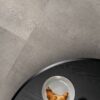 кварц-винил-quick-step-oro-concrete-rock Кварц-винил Quick-Step Oro Concrete Rock уложен на полу кухни — кухонный стол, на котором лежат круассан и чашка кофе.